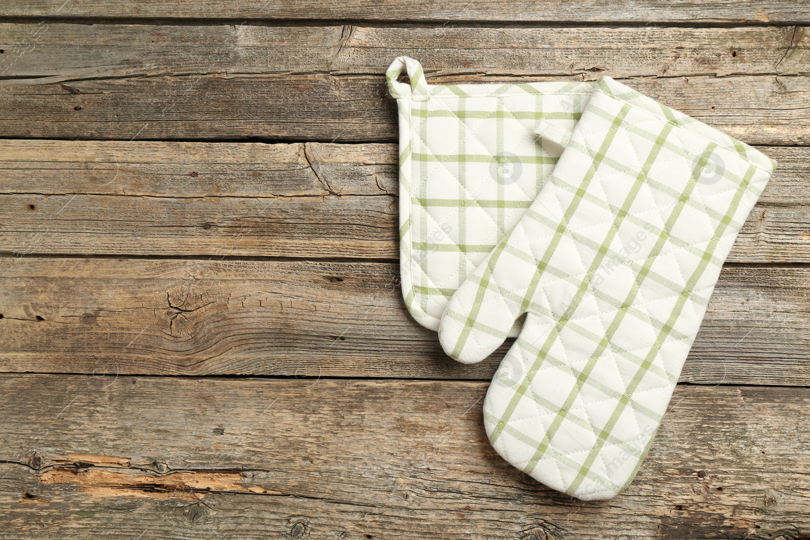 Photo of Oven glove and potholder on wooden table, top view. Space for text