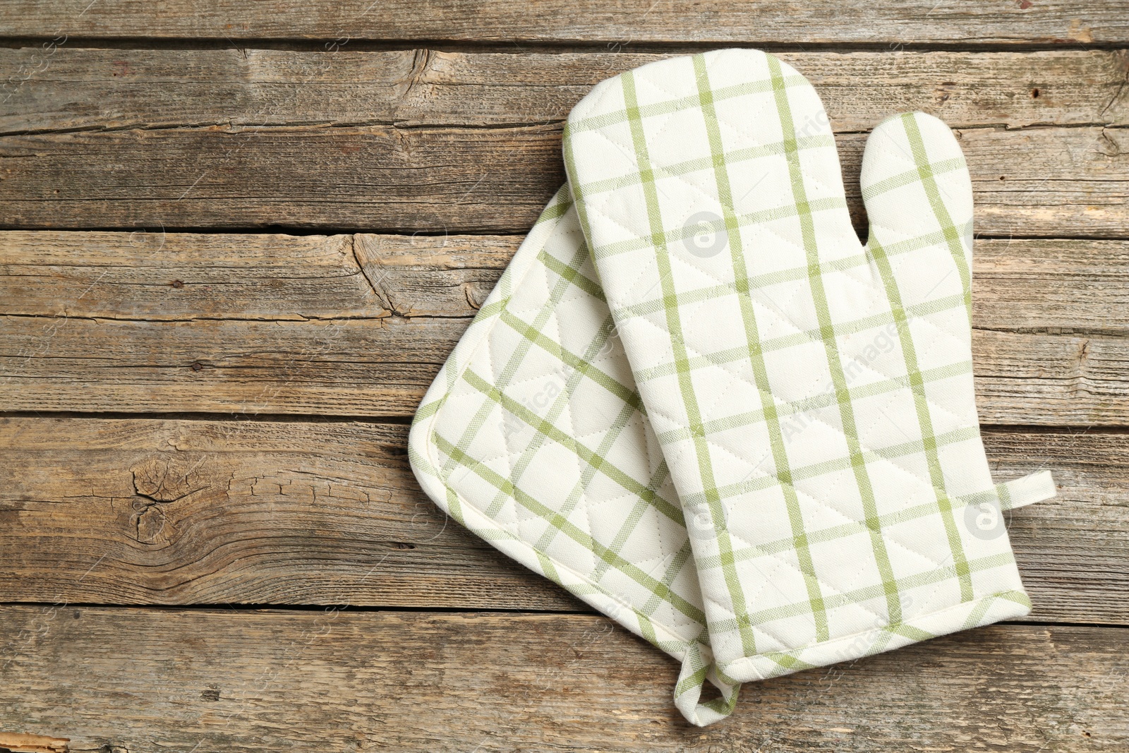 Photo of Oven glove and potholder on wooden table, top view. Space for text