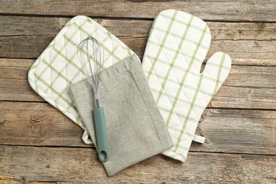 Photo of Oven glove and other kitchen utensils on wooden table, flat lay
