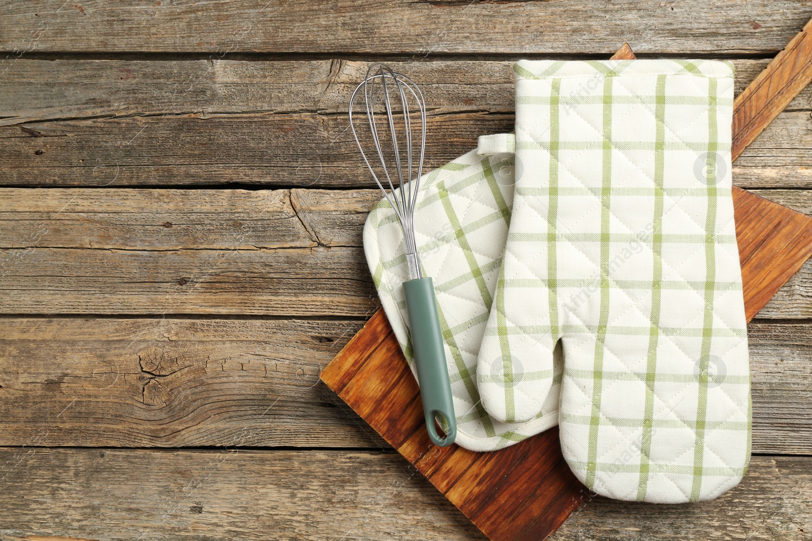 Photo of Oven glove and other kitchen utensils on wooden table, top view. Space for text