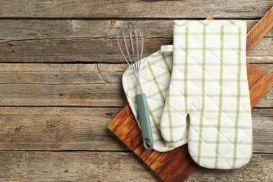 Photo of Oven glove and other kitchen utensils on wooden table, top view. Space for text