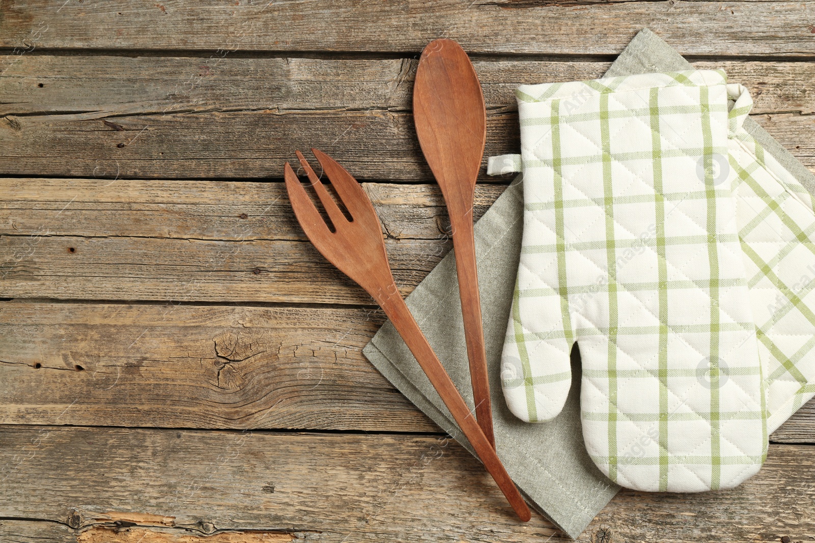 Photo of Oven glove and other kitchen utensils on wooden table, flat lay. Space for text