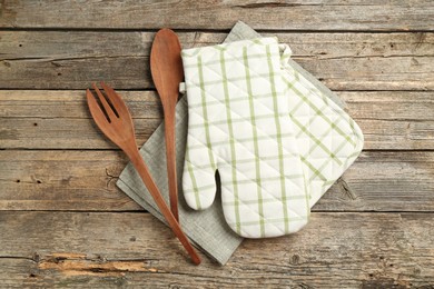 Photo of Oven glove and other kitchen utensils on wooden table, flat lay