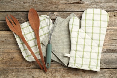 Photo of Oven glove and other kitchen utensils on wooden table, flat lay
