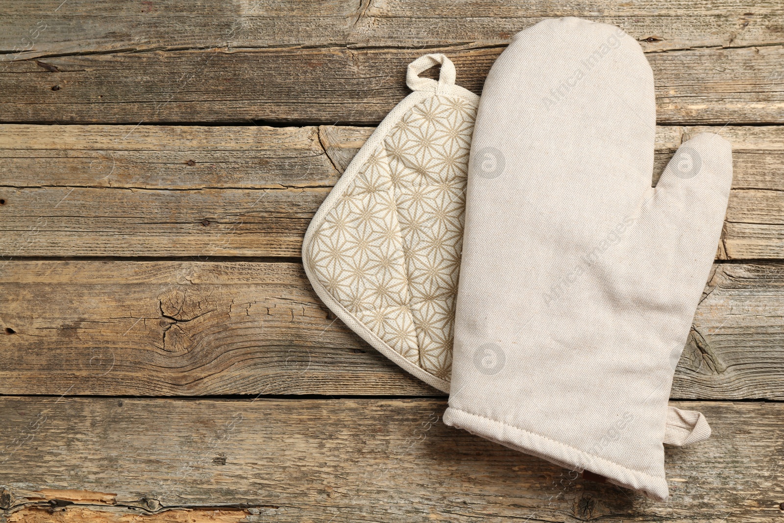 Photo of Oven glove and potholder on wooden table, top view. Space for text