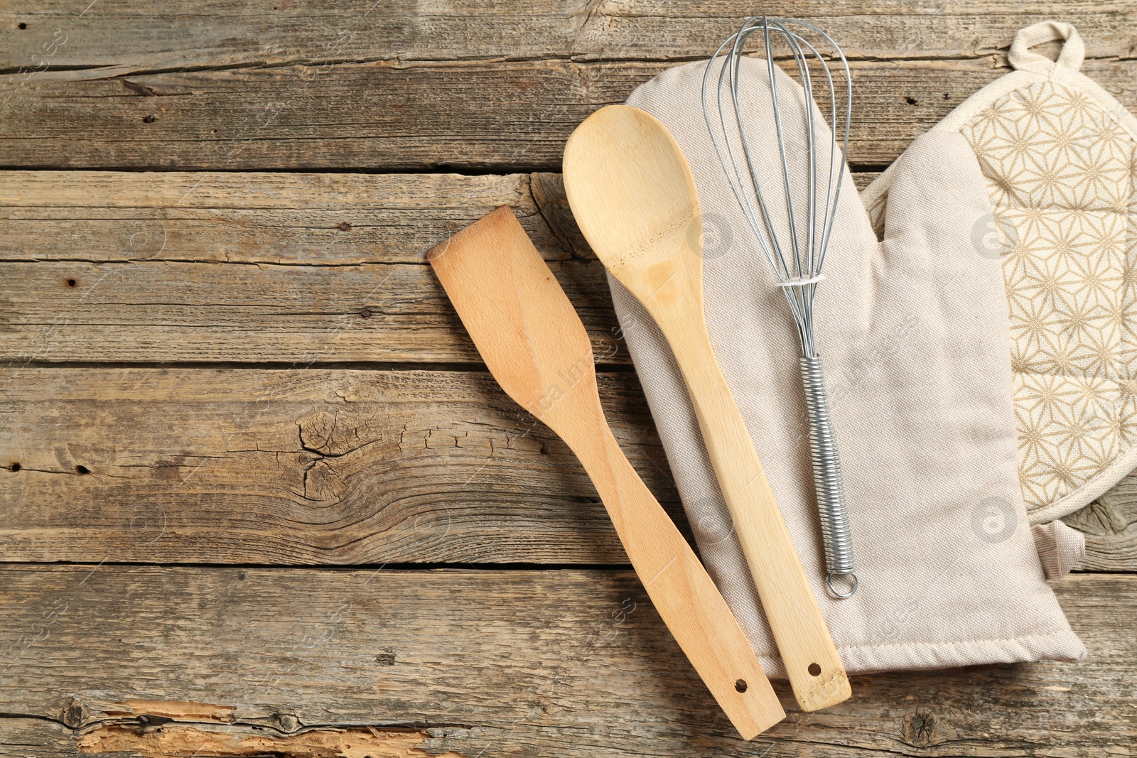 Photo of Oven glove and other kitchen utensils on wooden table, flat lay. Space for text