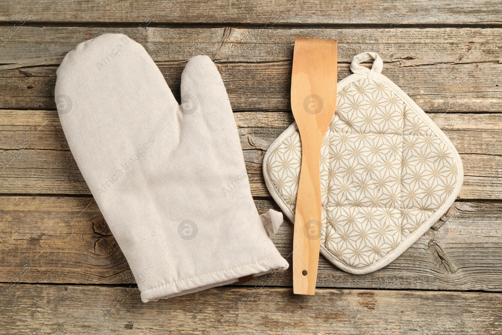 Photo of Oven glove, potholder and spatula on wooden table, flat lay