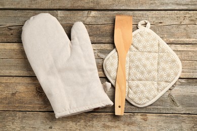 Photo of Oven glove, potholder and spatula on wooden table, flat lay