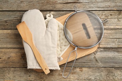 Photo of Oven glove and other kitchen utensils on wooden table, flat lay