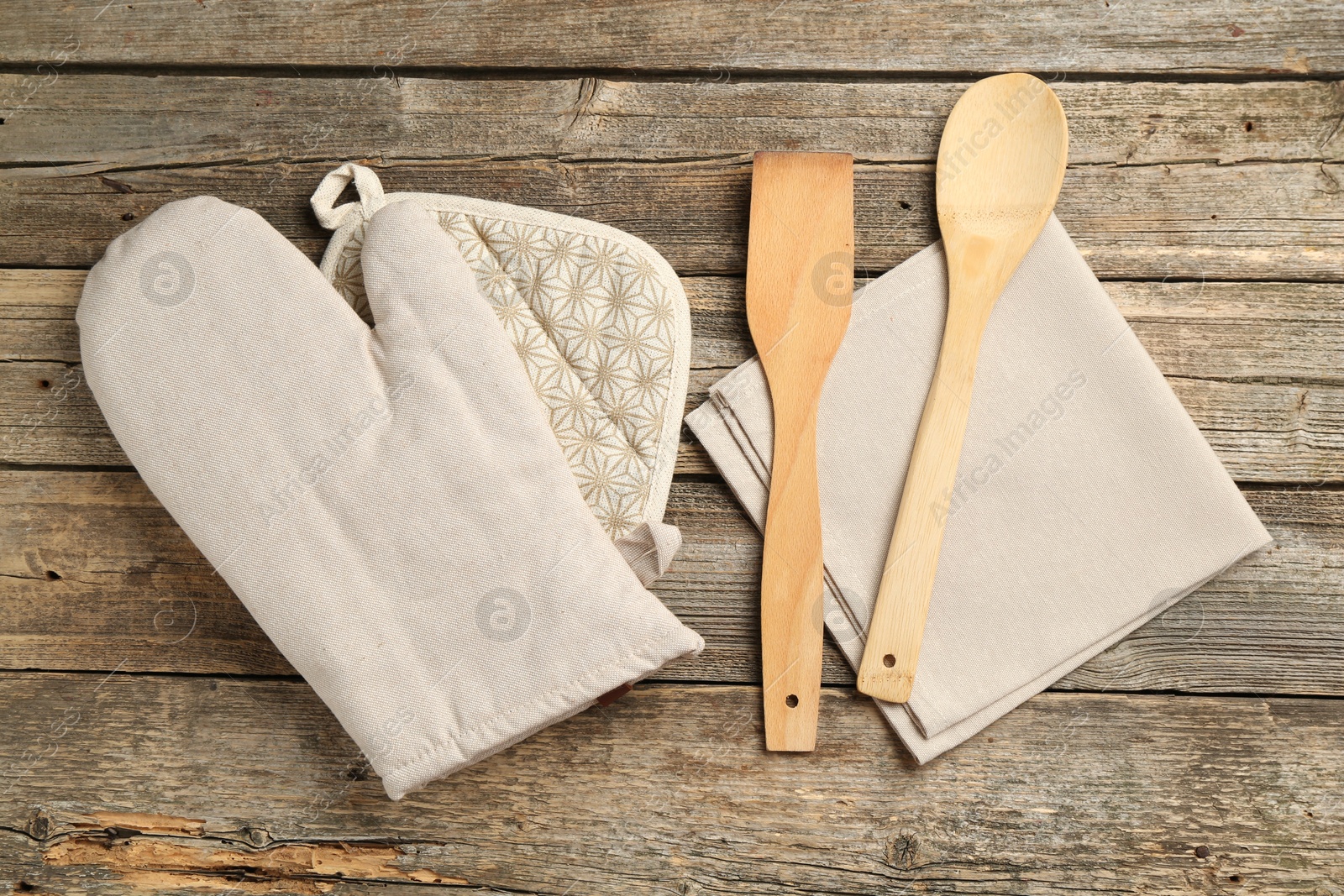 Photo of Oven glove and other kitchen utensils on wooden table, flat lay
