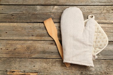 Photo of Oven glove, potholder and spatula on wooden table, flat lay. Space for text