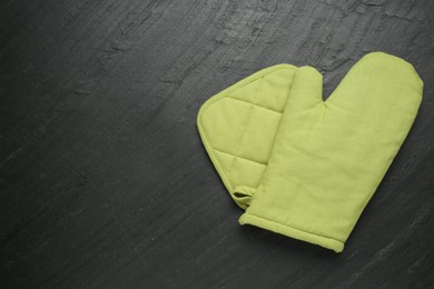 Photo of Green oven glove and potholder on dark textured table, top view. Space for text