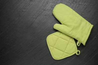 Photo of Green oven glove and potholder on dark textured table, flat lay. Space for text