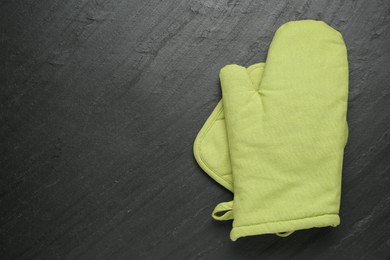 Photo of Green oven glove and potholder on dark textured table, top view. Space for text