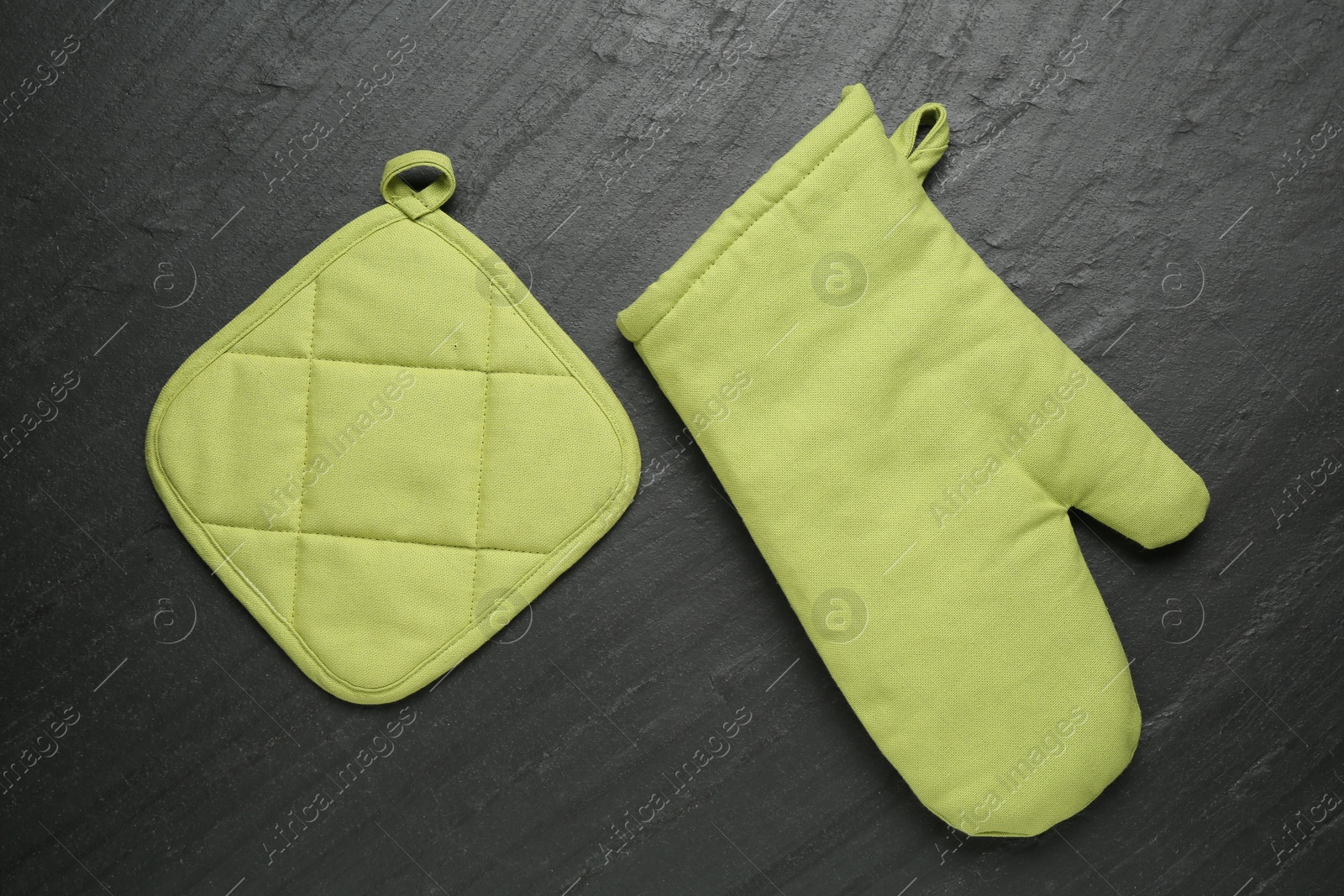 Photo of Green oven glove and potholder on dark textured table, flat lay