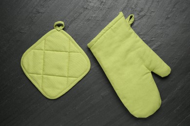 Photo of Green oven glove and potholder on dark textured table, flat lay