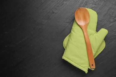 Photo of Green oven glove, wooden spoon and potholder on dark textured table, top view. Space for text