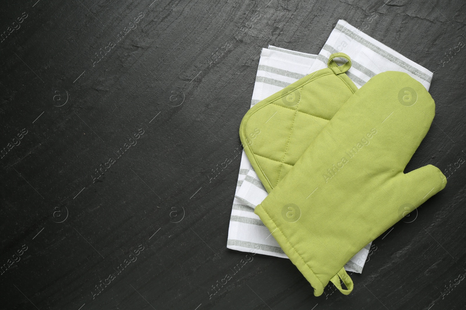 Photo of Green oven glove, towel and potholder on dark textured table, top view. Space for text