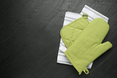 Photo of Green oven glove, towel and potholder on dark textured table, top view. Space for text