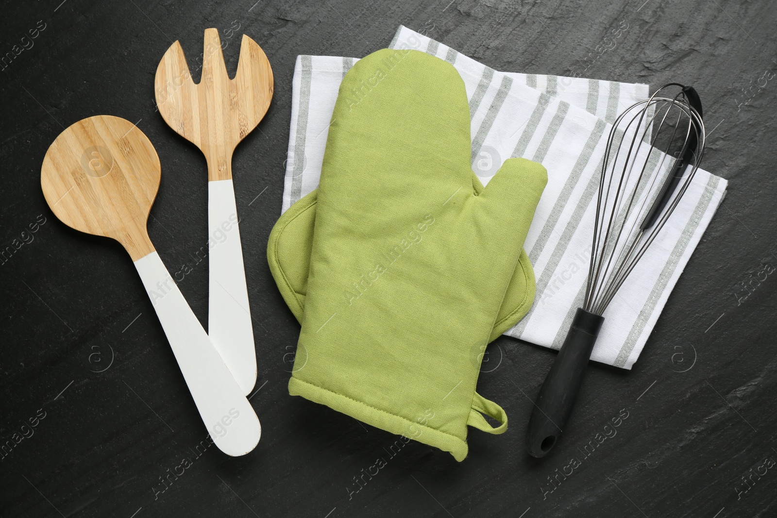 Photo of Green oven glove and other kitchen utensils on dark textured table, flat lay