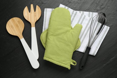 Photo of Green oven glove and other kitchen utensils on dark textured table, flat lay