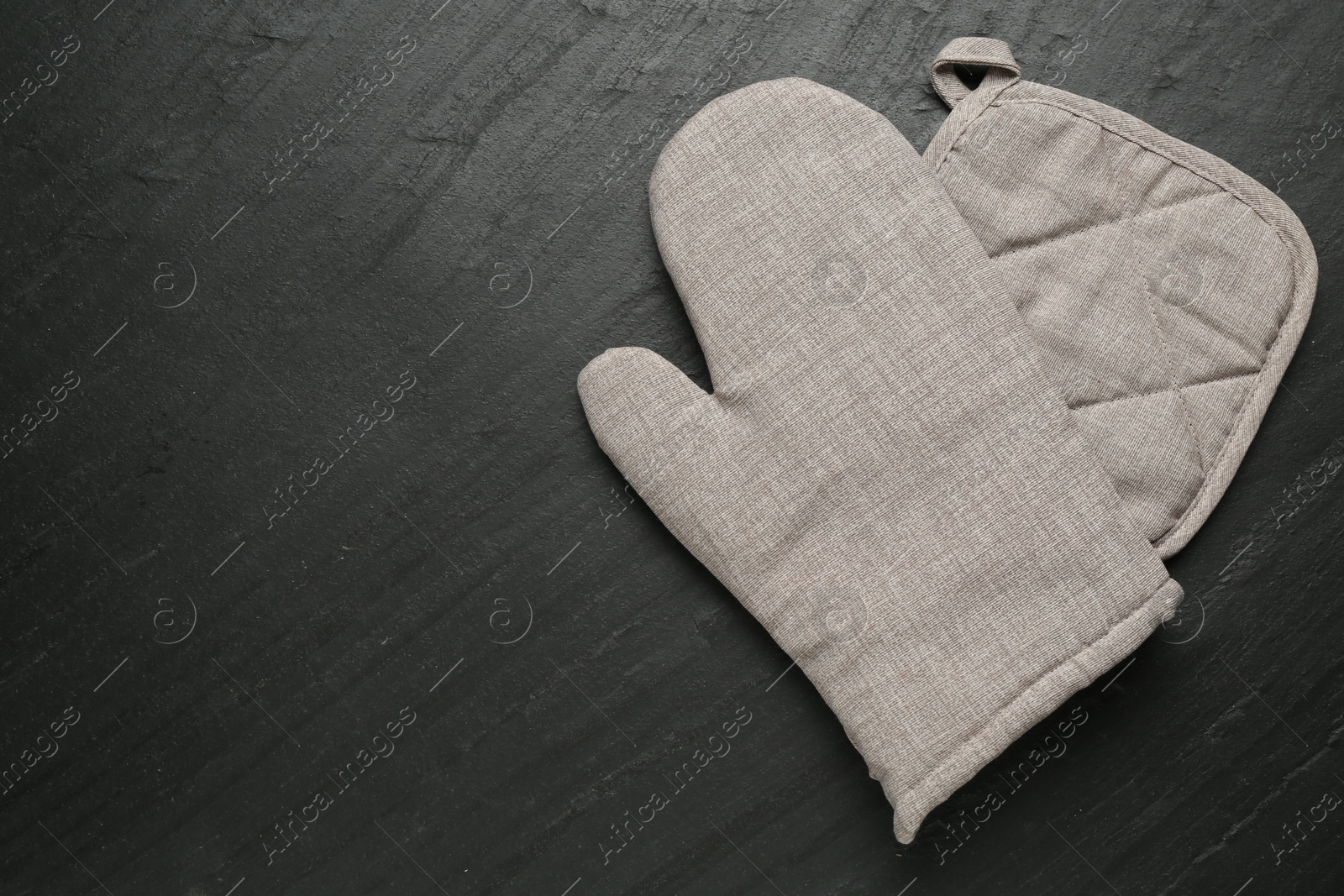 Photo of Grey oven glove and potholder on dark textured table, top view. Space for text