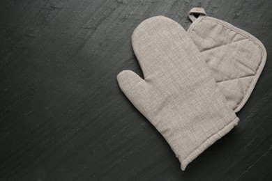 Photo of Grey oven glove and potholder on dark textured table, top view. Space for text