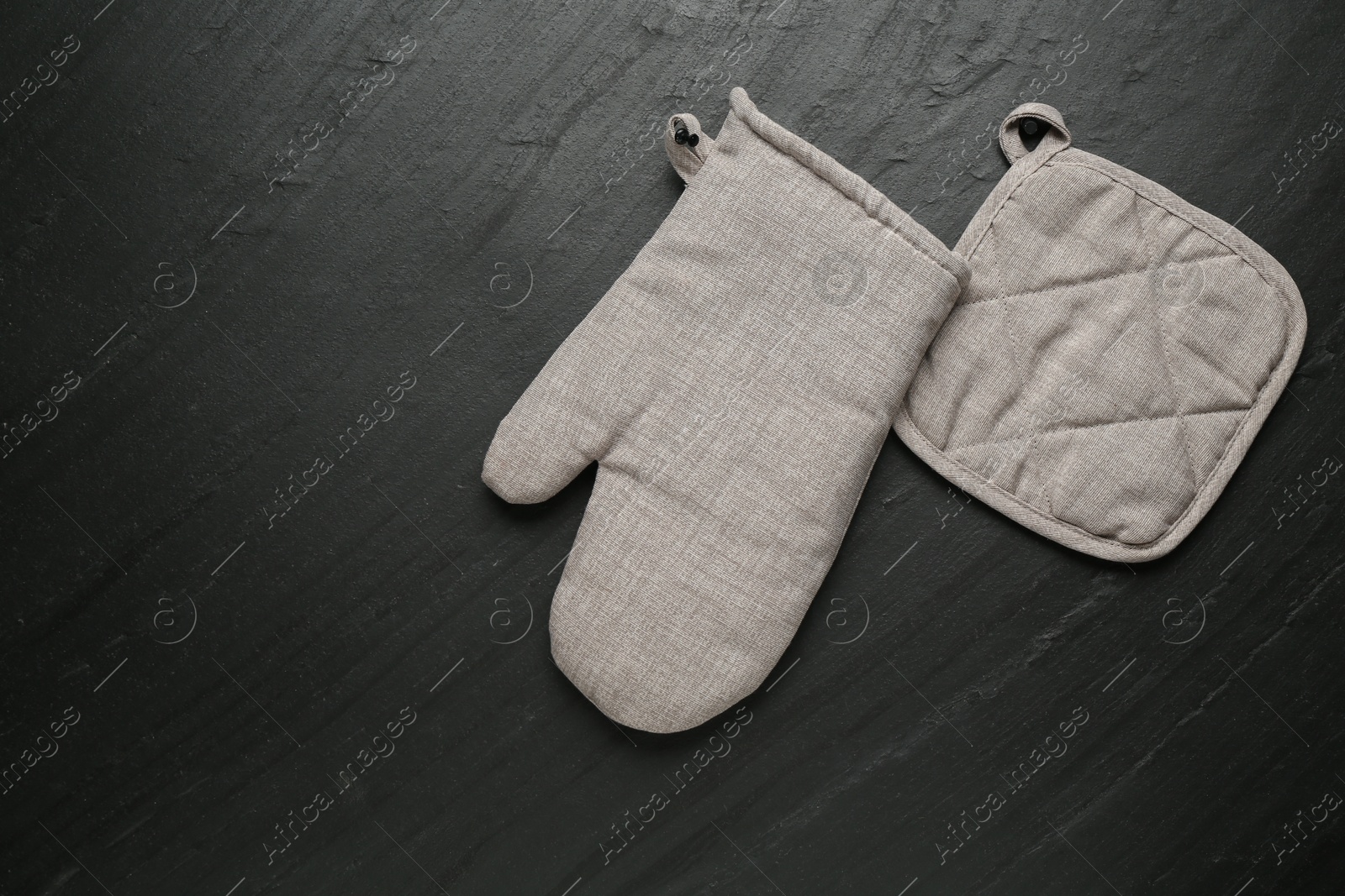 Photo of Grey oven glove and potholder on dark textured table, flat lay. Space for text