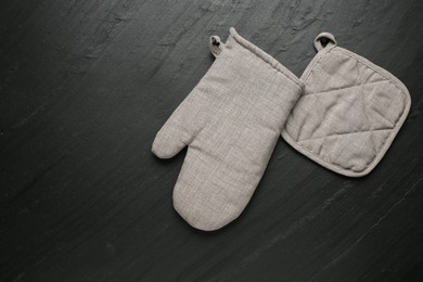 Photo of Grey oven glove and potholder on dark textured table, flat lay. Space for text
