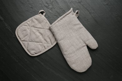 Photo of Grey oven glove and potholder on dark textured table, flat lay