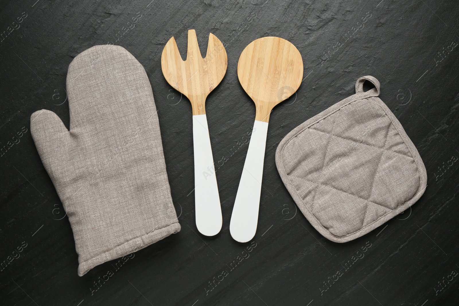 Photo of Grey oven glove and other kitchen utensils on dark textured table, flat lay