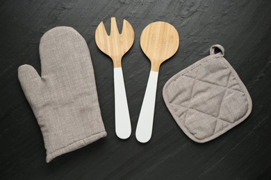 Photo of Grey oven glove and other kitchen utensils on dark textured table, flat lay