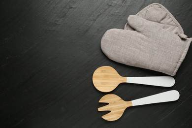 Photo of Grey oven glove and other kitchen utensils on dark textured table, flat lay. Space for text