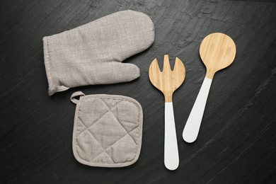 Photo of Grey oven glove and other kitchen utensils on dark textured table, flat lay