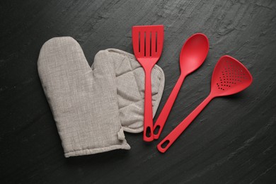 Photo of Grey oven glove and other kitchen utensils on dark textured table, flat lay
