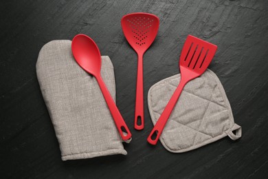 Photo of Grey oven glove and other kitchen utensils on dark textured table, flat lay