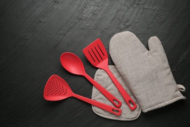 Photo of Grey oven glove and other kitchen utensils on dark textured table, flat lay