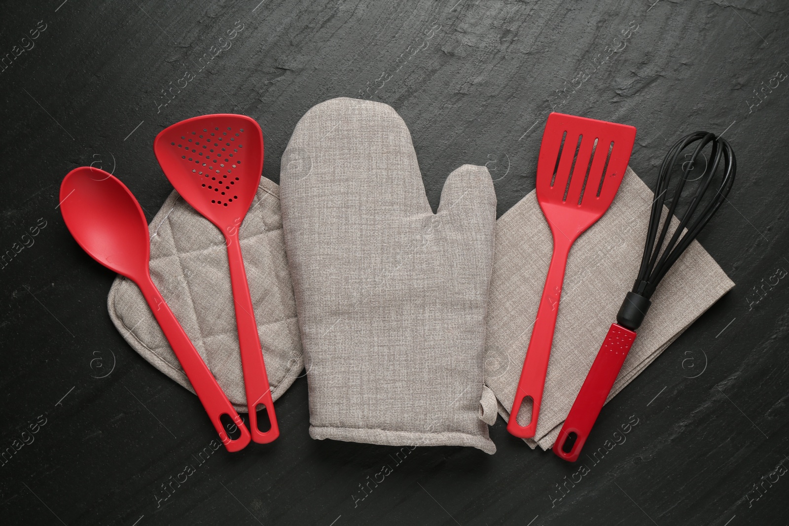 Grey oven glove and other kitchen utensils on dark textured table, flat lay Photo of Grey oven glove and other kitchen utensils on dark textured table, flat lay
