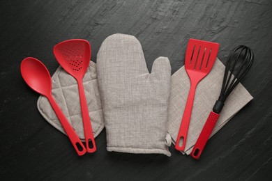 Photo of Grey oven glove and other kitchen utensils on dark textured table, flat lay