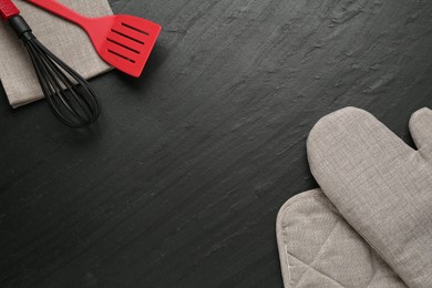 Photo of Grey oven glove and other kitchen utensils on dark textured table, flat lay. Space for text
