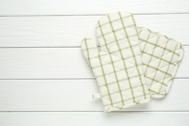 Photo of Oven glove and potholder on white wooden table, top view. Space for text