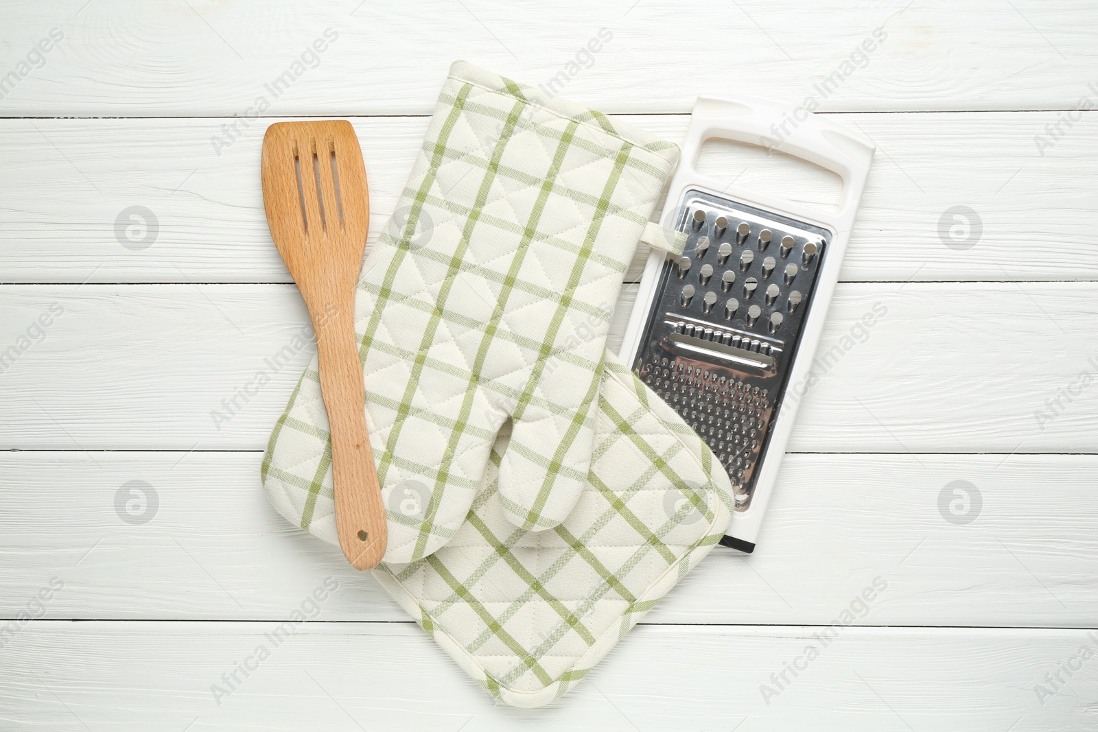 Photo of Oven glove, potholder, garter and spatula on white wooden table, flat lay