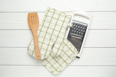 Photo of Oven glove, potholder, garter and spatula on white wooden table, flat lay