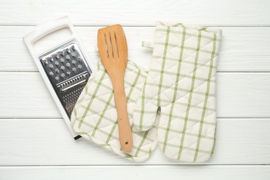 Photo of Oven glove, potholder, garter and spatula on white wooden table, flat lay