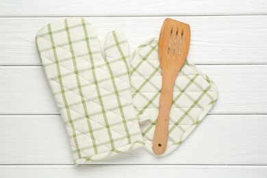 Photo of Oven glove, potholder and spatula on white wooden table, flat lay
