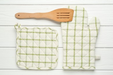 Photo of Oven glove, potholder and spatula on white wooden table, flat lay