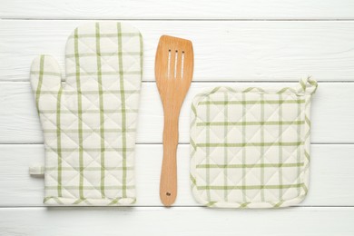 Photo of Oven glove, potholder and spatula on white wooden table, flat lay