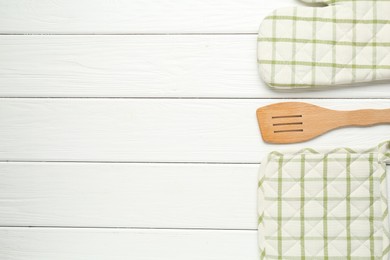 Photo of Oven glove, potholder and spatula on white wooden table, flat lay. Space for text