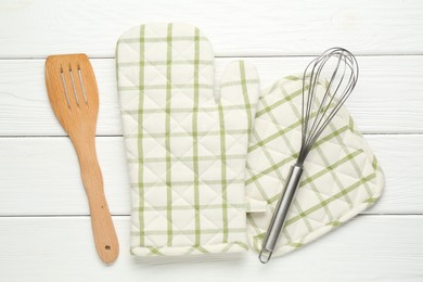 Photo of Oven glove, potholder, whisk and spatula on white wooden table, flat lay