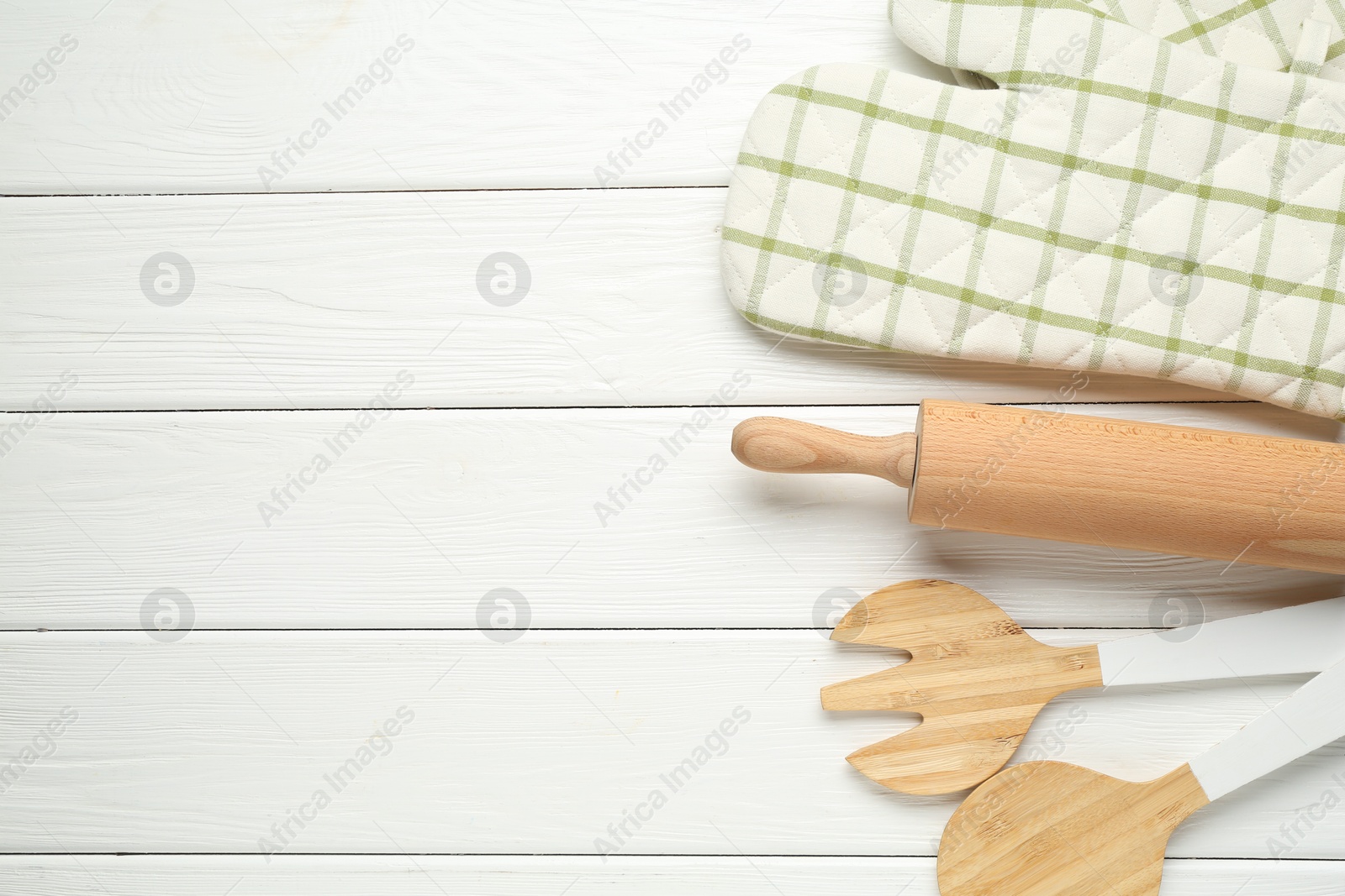 Photo of Oven glove and other kitchen utensils on white wooden table, flat lay. Space for text